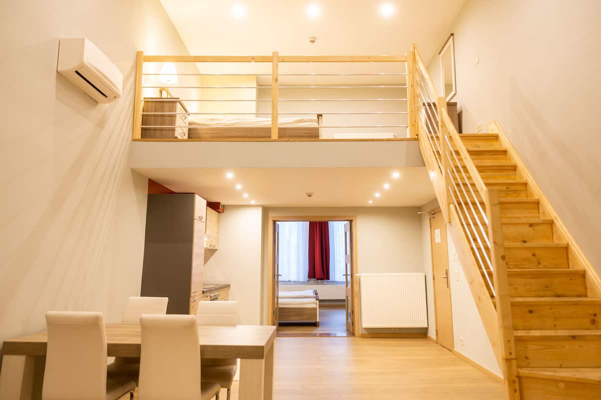 A modern, well-lit room with a wooden staircase, a bunk bed, a dining area with chairs, and a kitchen area.