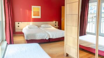 A hotel room with two beds, a red wall, and a window with curtains.