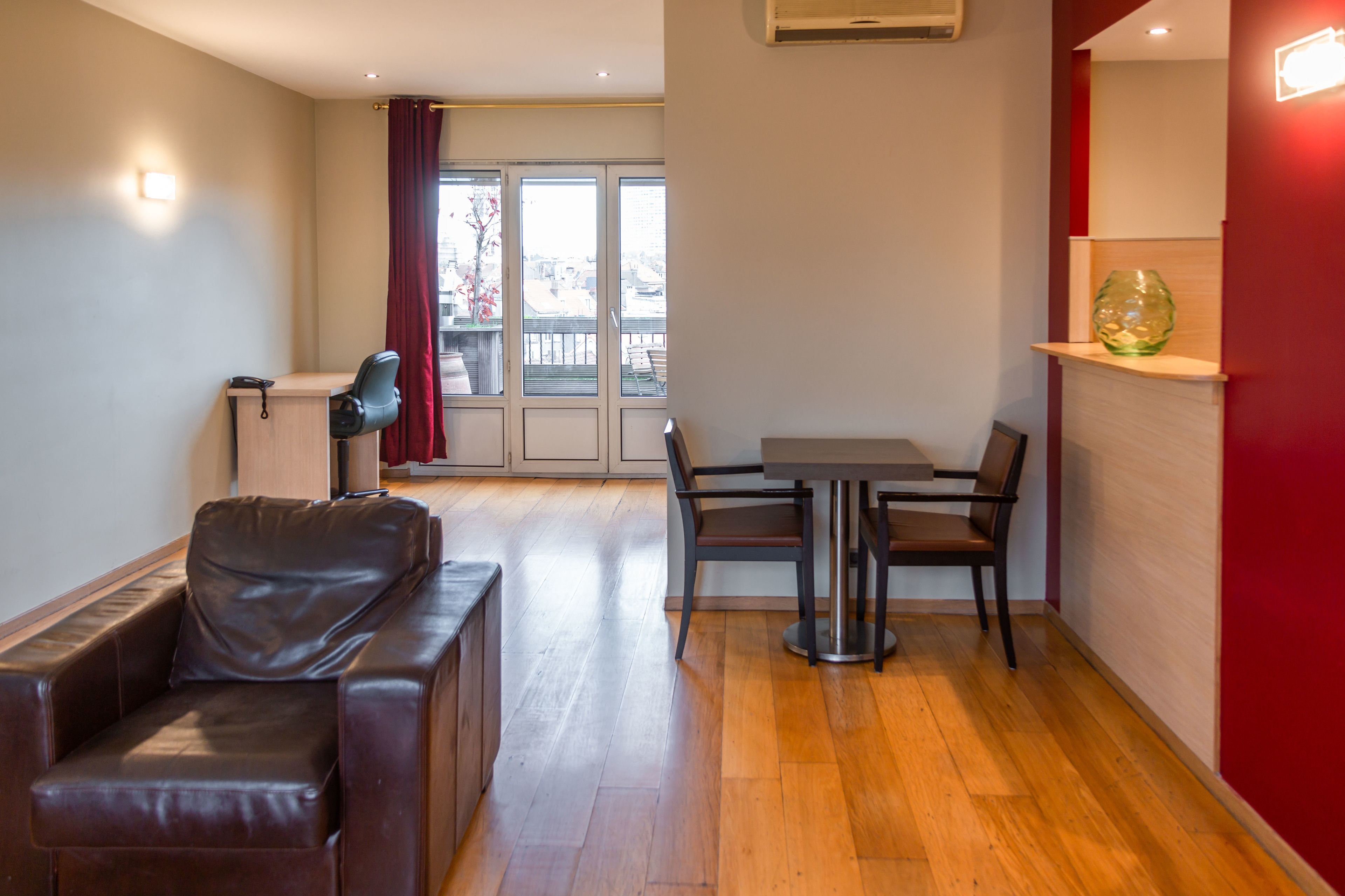 Una sala moderna con un sofá de cuero, una mesa de comedor con sillas y una pared de acento roja.