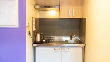 A compact kitchen with stainless steel appliances, a kettle, and a sink.