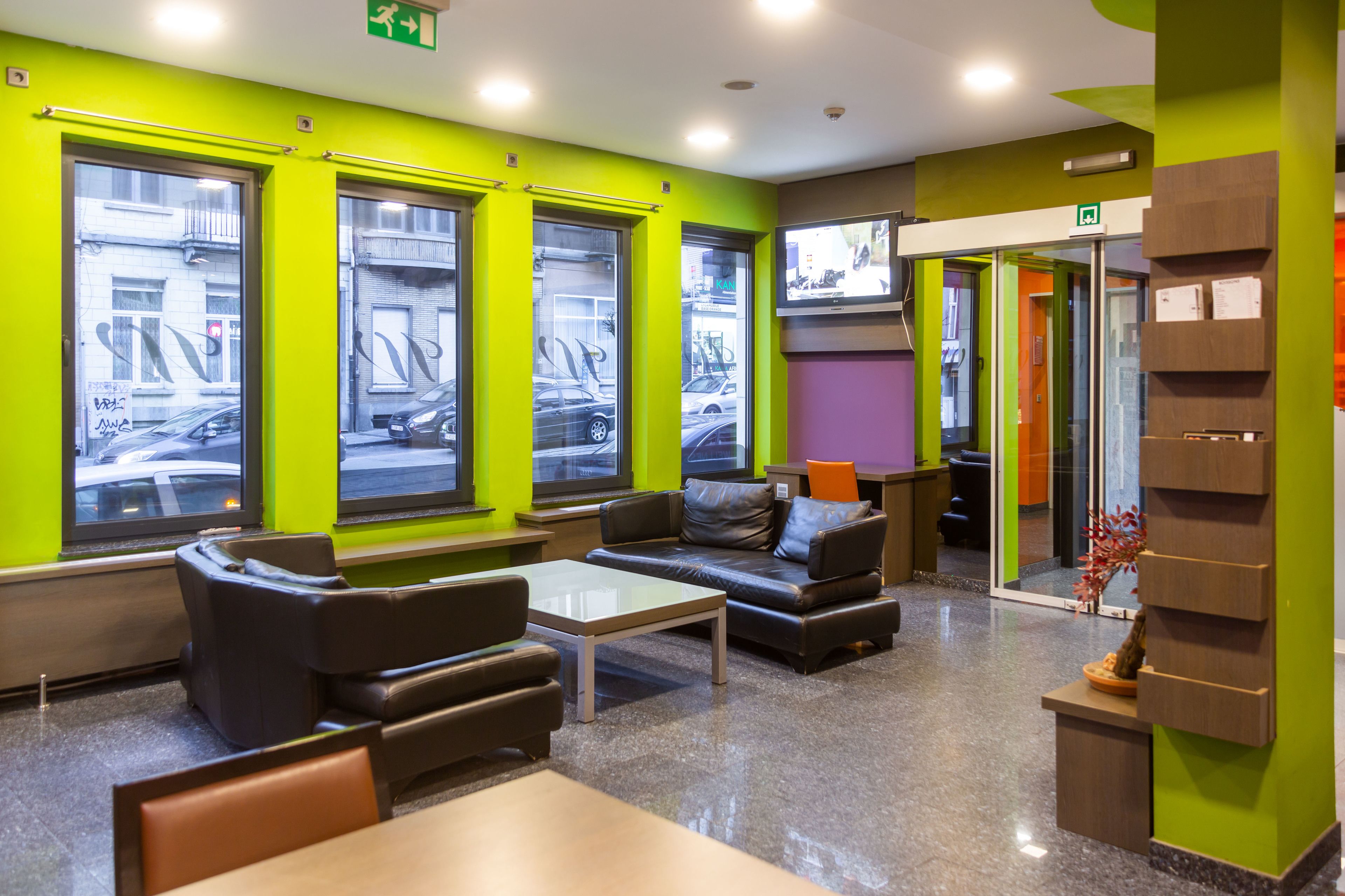 Un moderno hall con paredes verdes, asientos de cuero, una mesa de centro y un televisor montado en la pared.