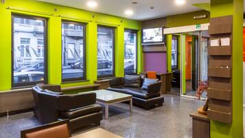 Un moderno hall con paredes verdes, asientos de cuero, una mesa de centro y un televisor montado en la pared.