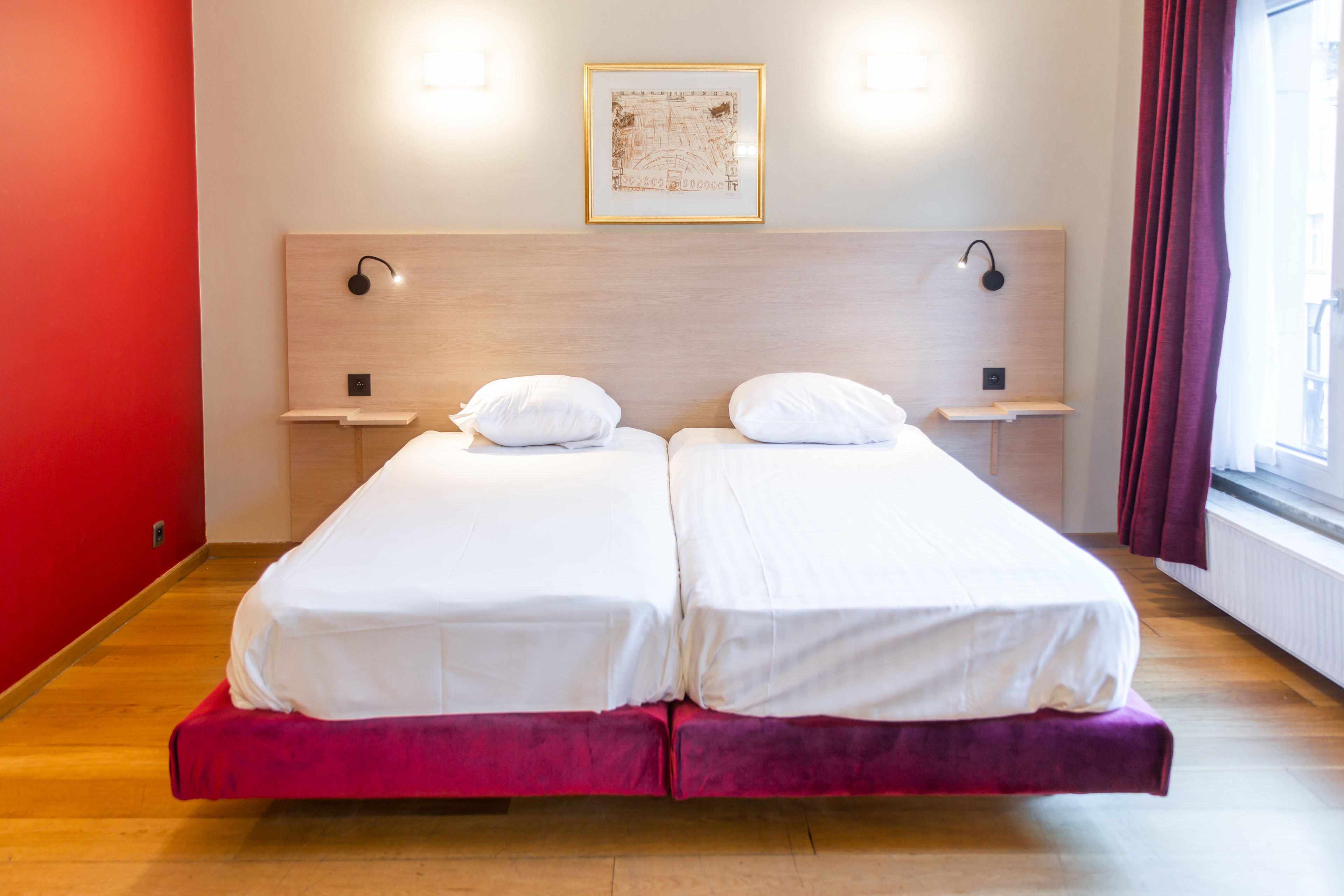 Ein Doppelbett mit weißer Bettwäsche, zwei Nachttische, ein gerahmtes Bild an der Wand und ein Fenster mit Vorhängen.