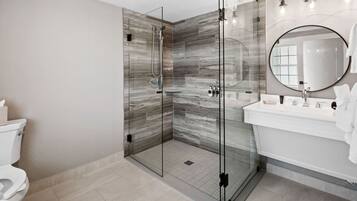 Un baño moderno con ducha envuelta en vidrio, un lavamanos blanco y un espejo grande.