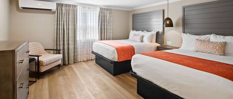 A hotel room with two beds, a desk, a chair, and an air conditioning unit.