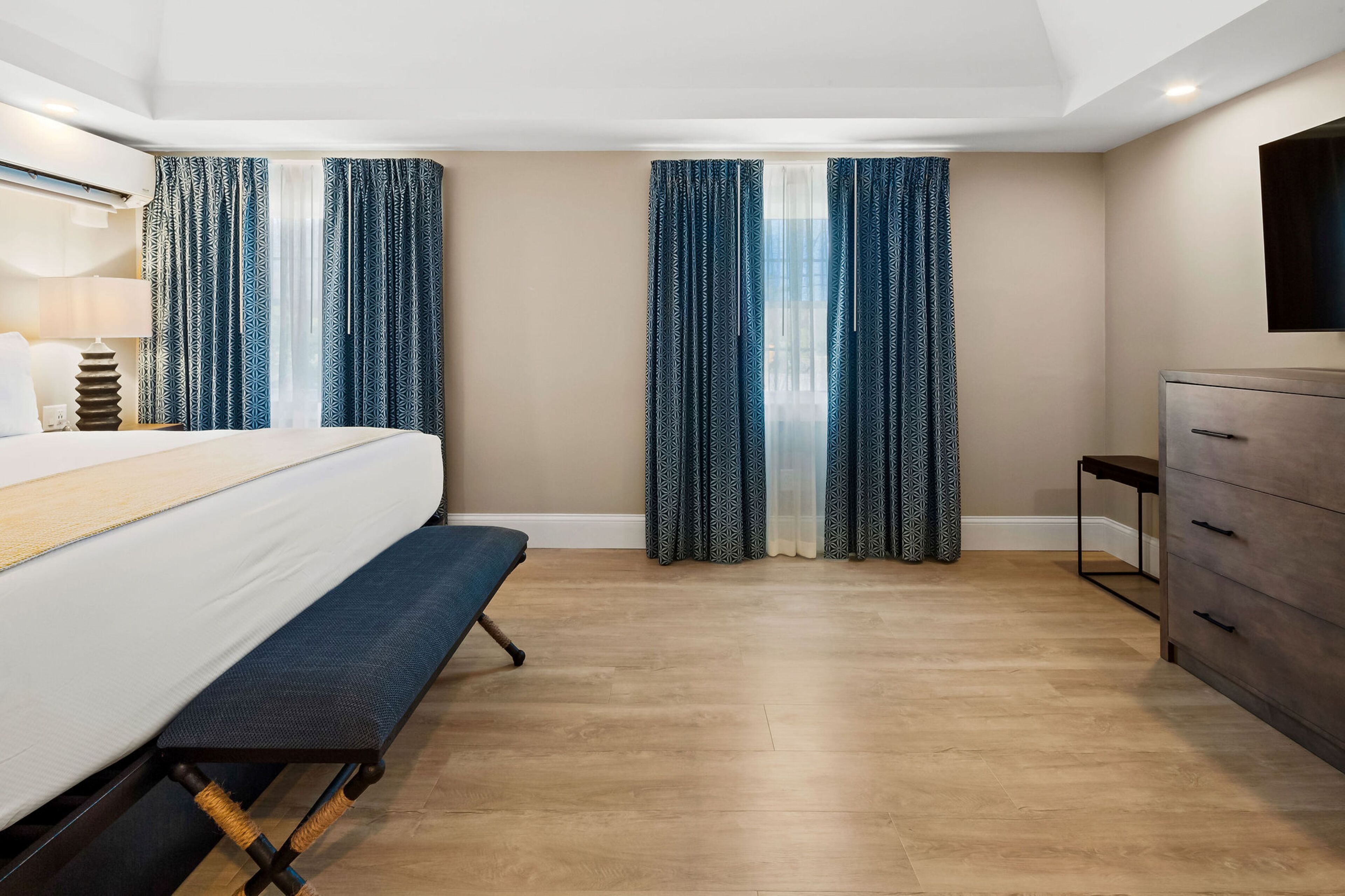 A modern hotel room with a large bed, a bench, a dresser, and a TV mounted on the wall.