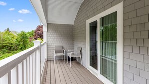 A covered balcony with a white railing, grey siding, and a glass door leading to the interior. - Love Farms Lodge (West Dennis)