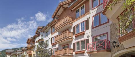 Una hilera de edificios de varios pisos con balcones, un patio central y montañas al fondo.