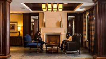 A lobby with a fireplace, two blue armchairs, and a black leather sofa.