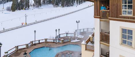 A hotel with a pool area, including a hot tub and a small pool, surrounded by snowy landscape and ski slopes.
