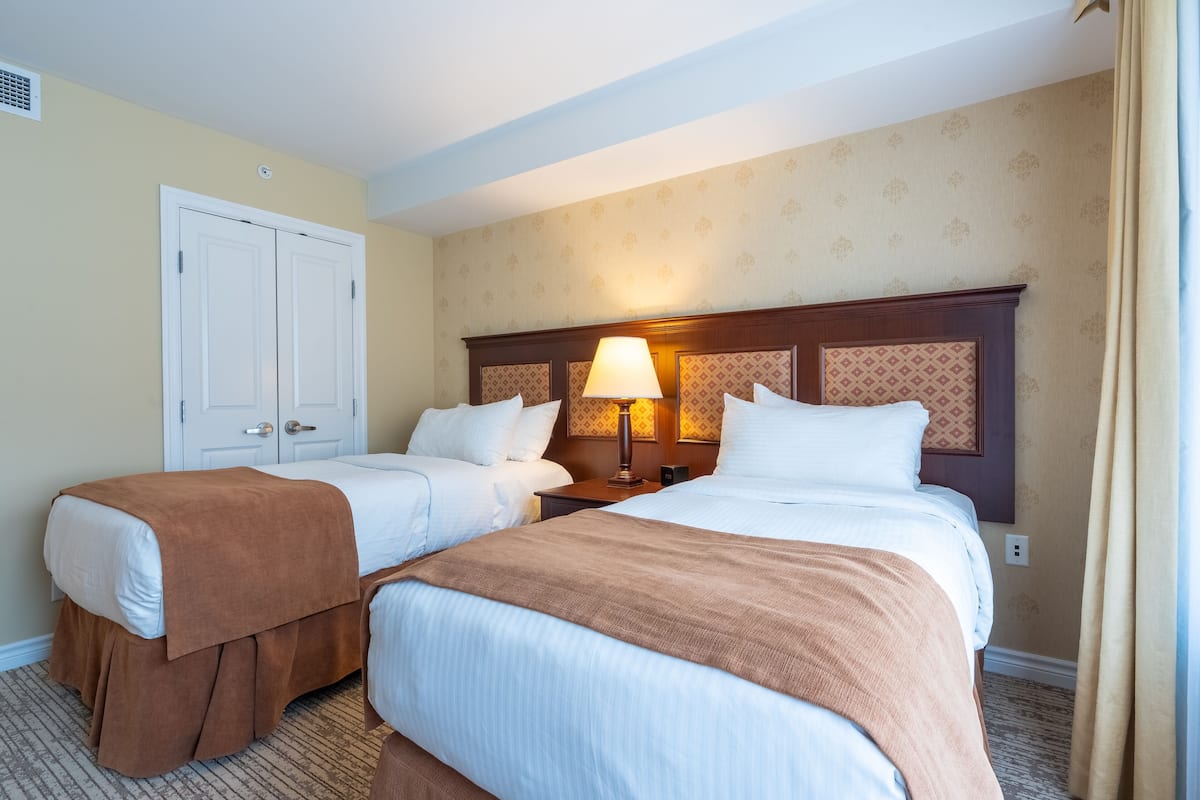 A hotel room with two beds, a wooden headboard, a nightstand, and a lamp.