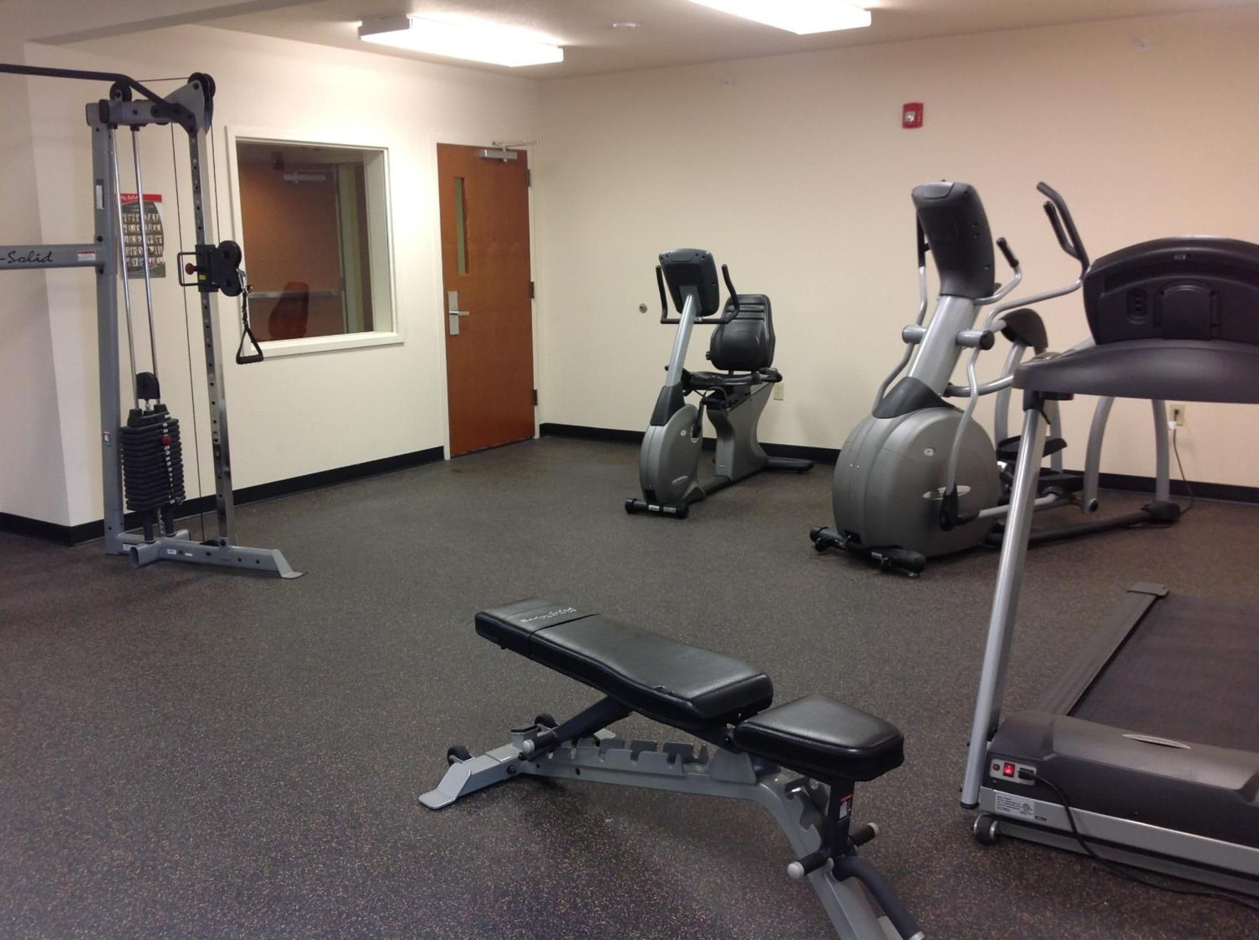 A gym with a bench press, elliptical, and treadmills.