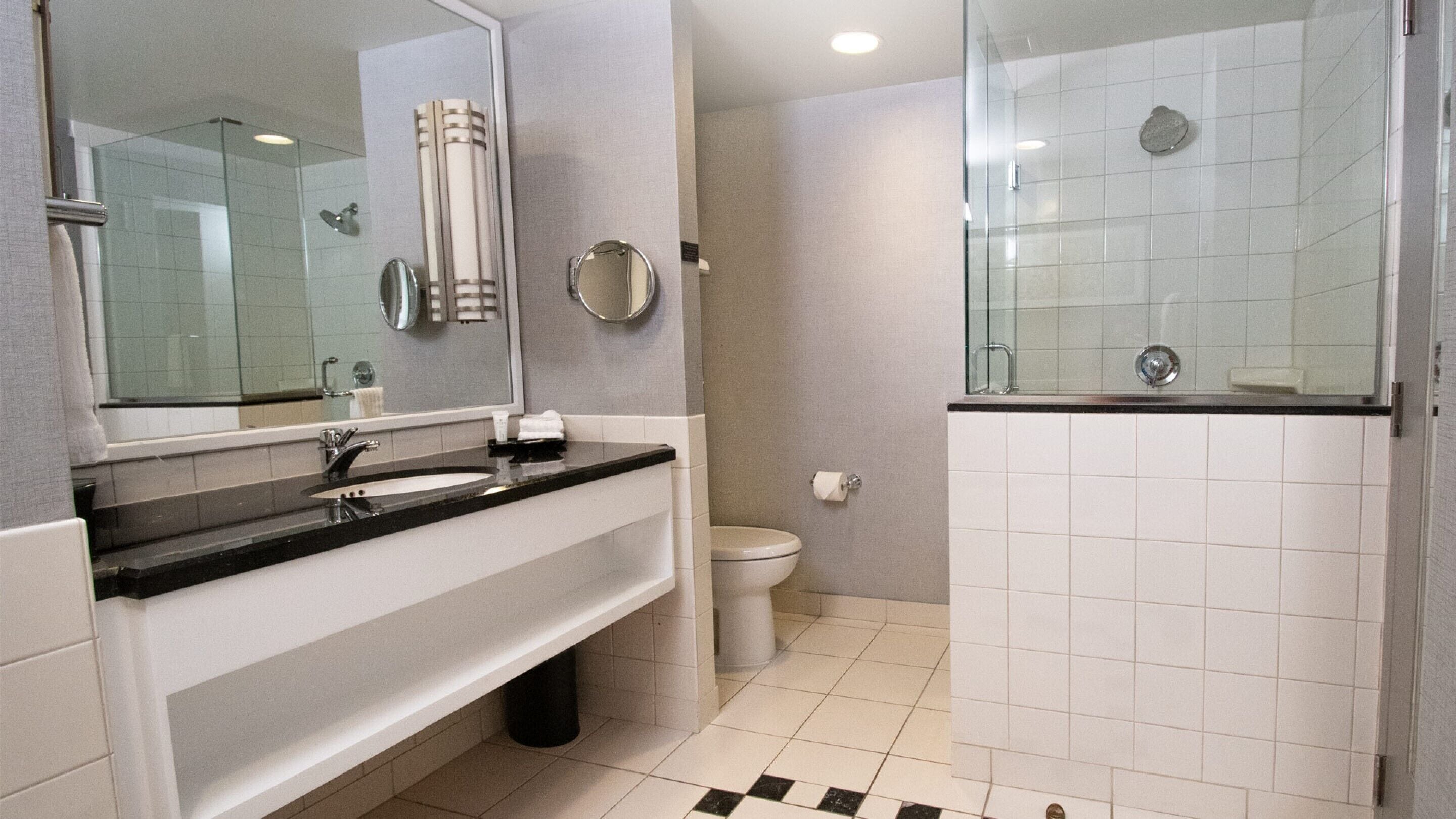 A modern bathroom with a black countertop sink, a large mirror, a toilet, and a glass-enclosed shower area.