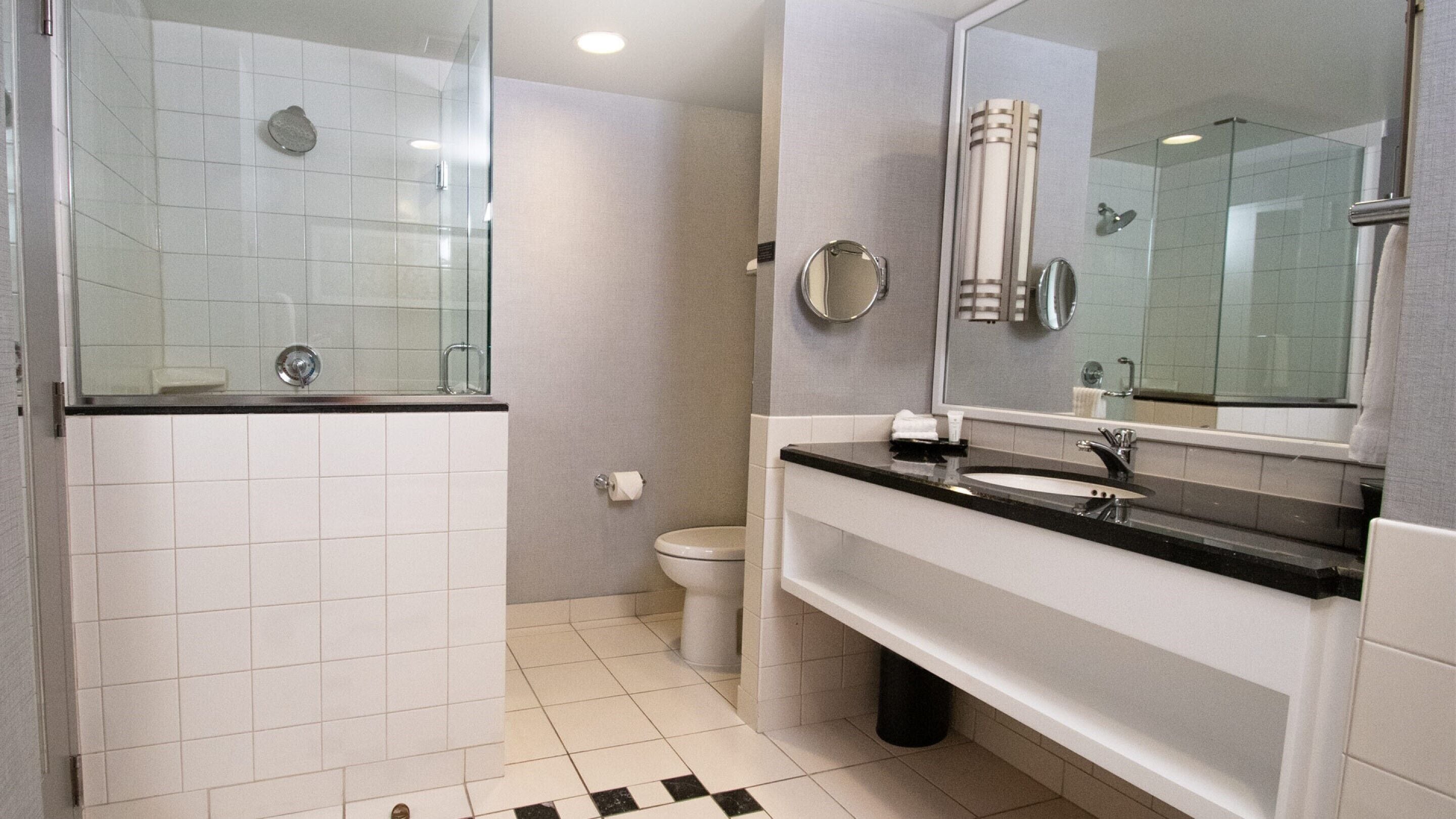 Een moderne badkamer met een douchecabine van glas, een wit toilet, een wastafel met spiegel en een zwart-wit geruite vloer.
