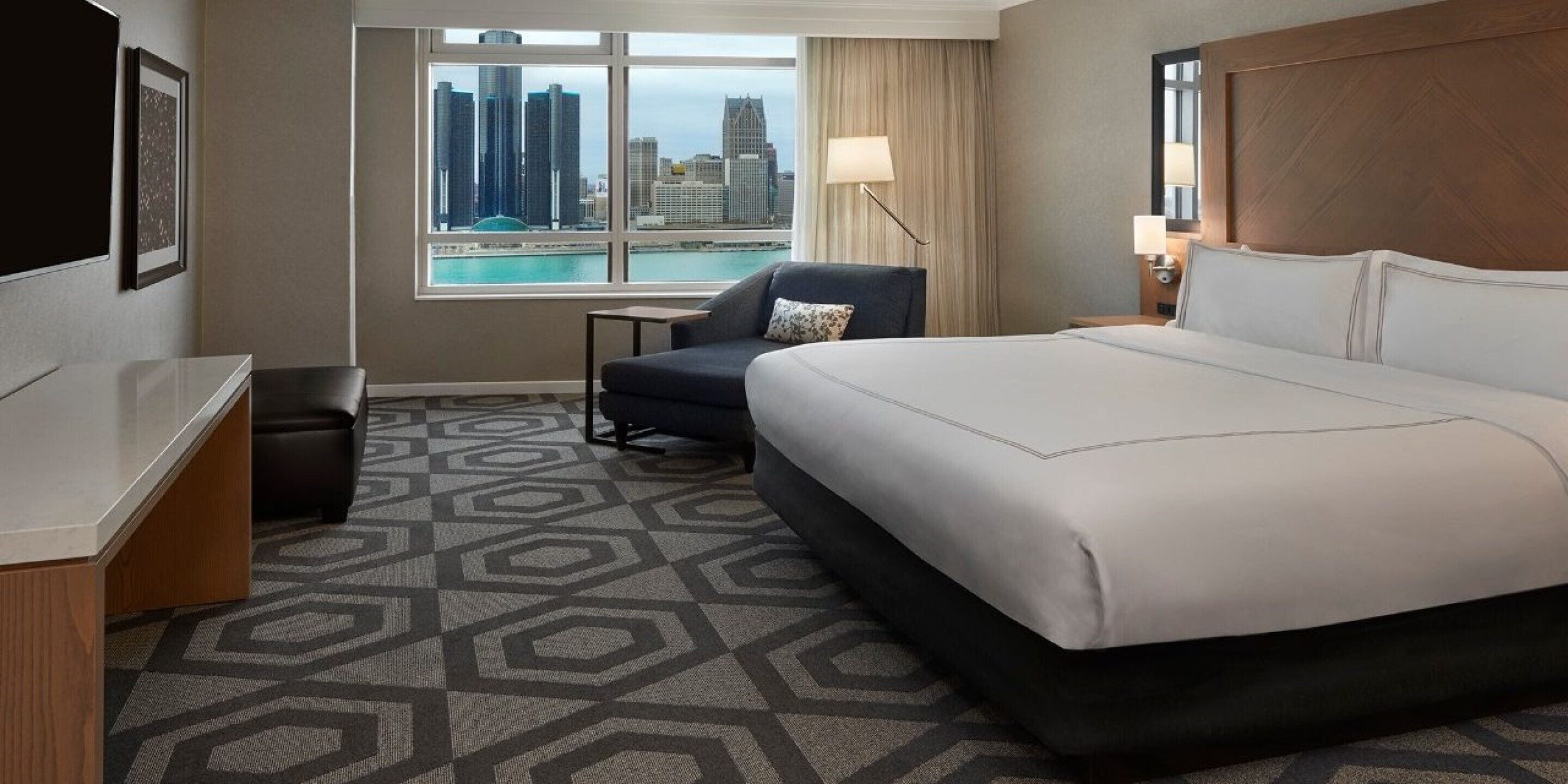 Une chambre d’hôtel avec un grand lit, un bureau, une chaise et une vue sur les toits de la ville par la fenêtre.