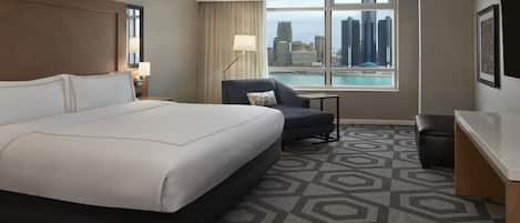 Habitación de hotel con una cama grande, un escritorio, una silla, vistas de la ciudad y una alfombra estampada.