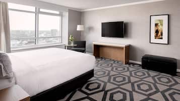A hotel room with a large bed, a desk, a TV, and a city view.