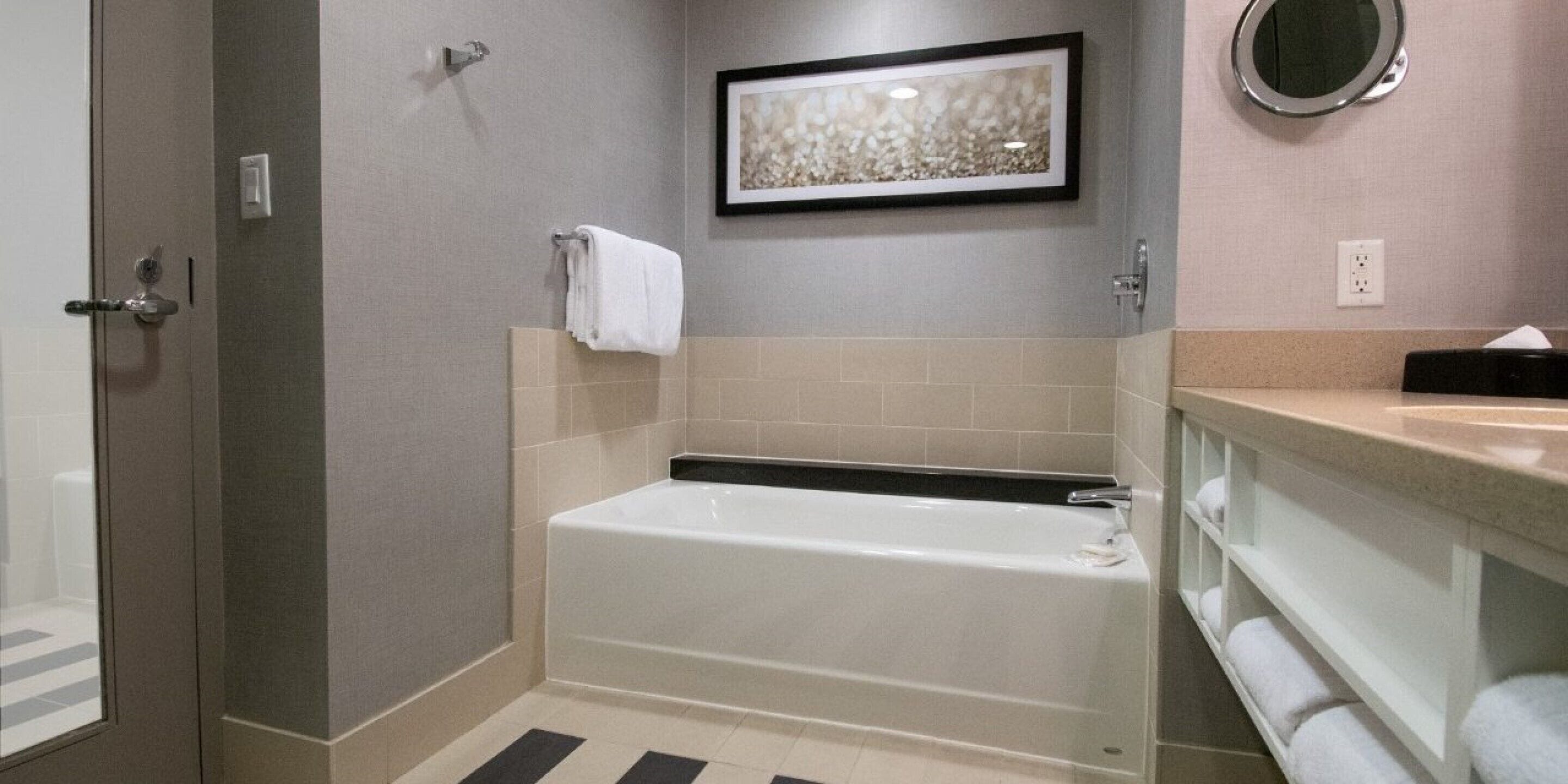 A modern bathroom with a bathtub, a framed artwork above the tub, and a towel rack.