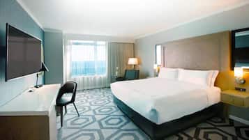 A hotel room with a large bed, a desk with a chair, a TV, and a window with curtains.
