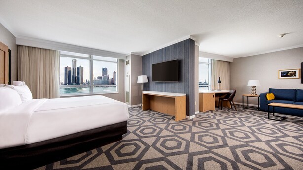 A hotel room with a large bed, a desk, a TV, and a view of a city skyline. - Caesars Windsor Hotel & Casino - A Caesars Rewards Destination (Windsor)