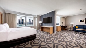 A hotel room with a large bed, a desk, a TV, and a view of a city skyline.