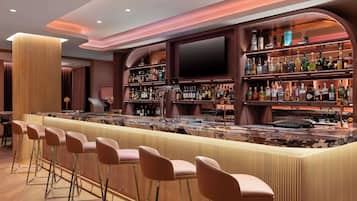 Zona de bar con una barra alargada, varios taburetes y estantes llenos de botellas.