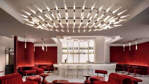 A modern bar area with red seating, a wine display, and a unique ceiling light fixture. - Revery Toronto Downtown, Curio Collection by Hilton (Toronto)