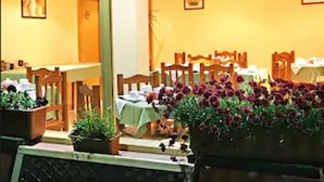 Un comedor con mesas y sillas, plantas en macetas e imágenes enmarcadas en las paredes.