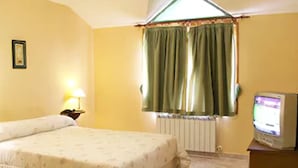 Una habitación con una cama, un escritorio, una lámpara, un ventanal con cortinas y un televisor.