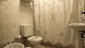 Baño con inodoro, bidé, lavamanos y cortina de ducha.