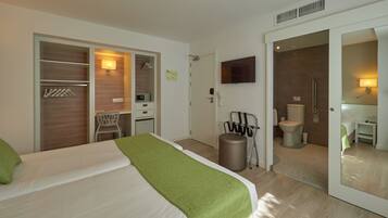 Habitació d'hotel amb llit, escriptori, cadira, televisió, dutxa i vàter.