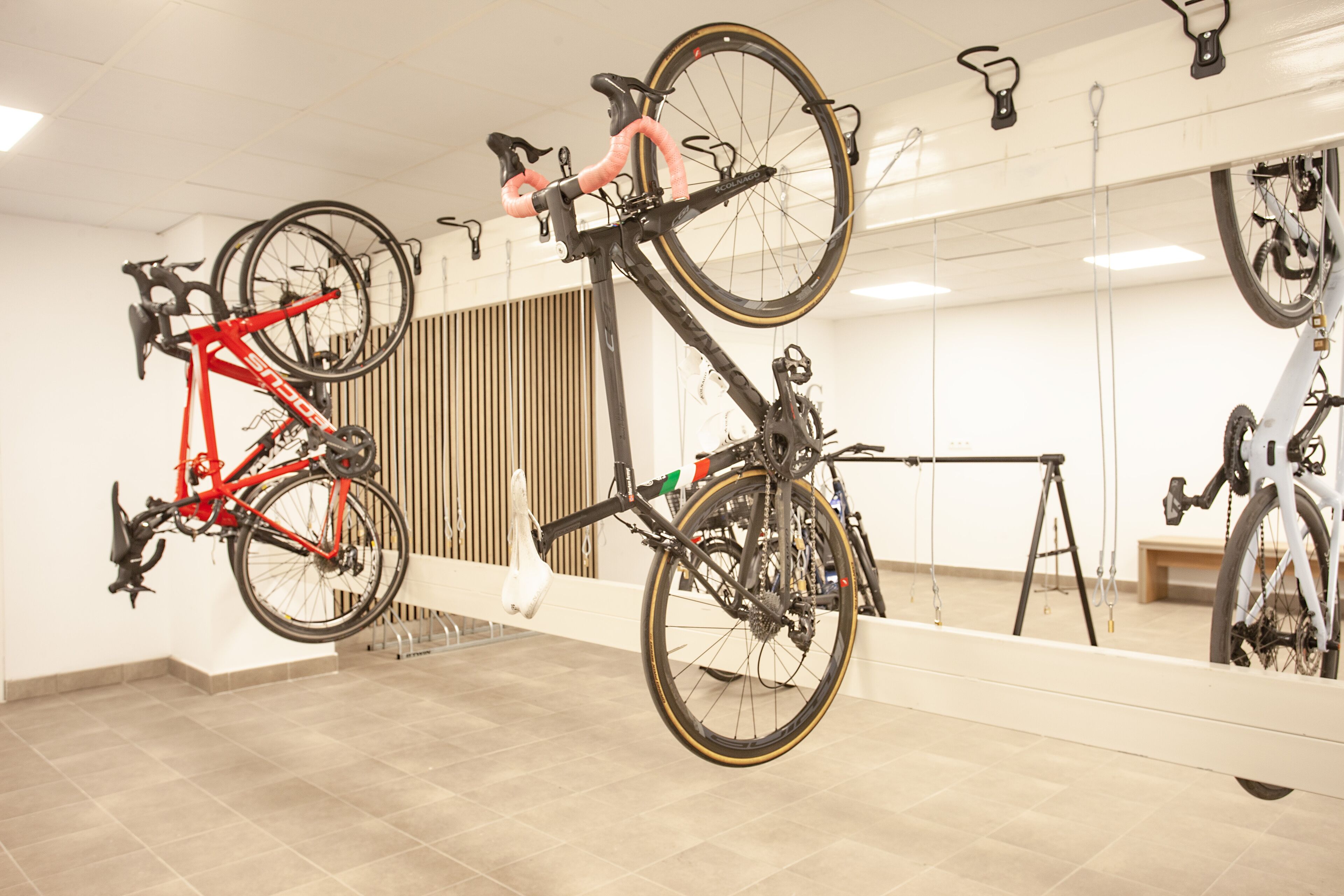 Una habitación con bicicletas colgadas en una pared, un banco de madera y un espejo grande que refleja las bicicletas.