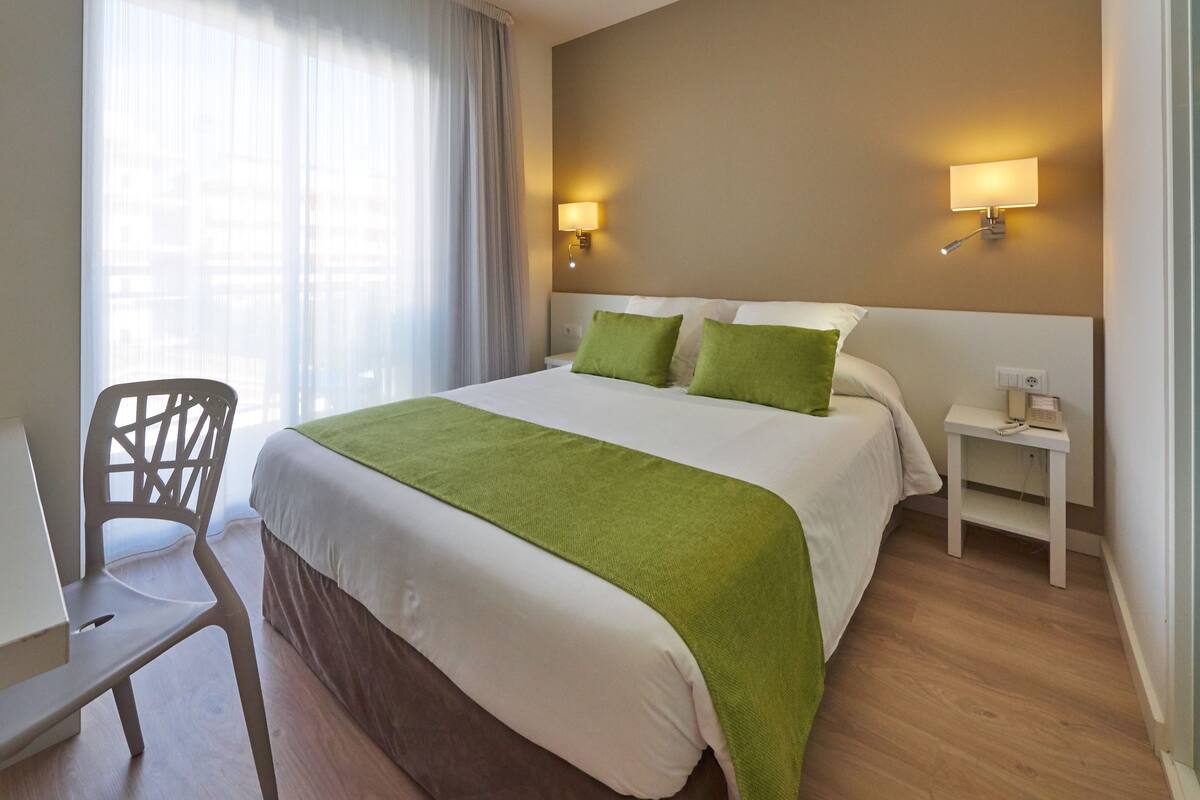 A hotel room with a bed, a chair, a nightstand, and a lamp.