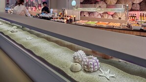 A seafood display with various shellfish and starfish, a chef preparing food, and a wall decorated with umbrellas.