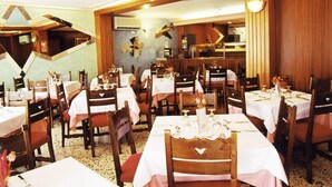 Un restaurant doté de nombreuses tables et chaises, avec une cuisine visible au fond et des murs recouverts de lambris en bois.