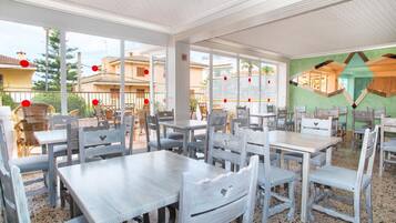 Un comedor interior con varias mesas y sillas, ventanas amplias y vistas a los edificios exteriores.