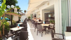 An outdoor cafe area with tables and chairs, surrounded by greenery and palm trees. - Maracaibo (Santa Margalida)