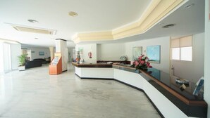 A modern reception area with a curved reception desk, a small seating area, and a large window providing natural light. - Maracaibo (Santa Margalida)