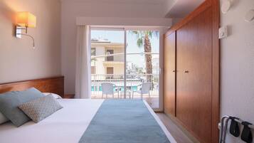 Een hotelkamer met een bed, een nachtkastje, een wandlamp, een schuifdeur naar een balkon met stoelen en een houten garderobe.