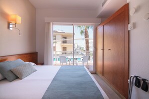 Een hotelkamer met een bed, een nachtkastje, een wandlamp, een schuifdeur naar een balkon met stoelen en een houten garderobe.