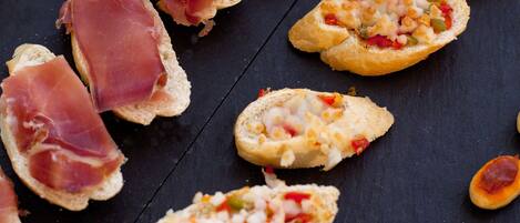 Une variété de hors-d'œuvre, notamment du pain accompagné de fromage et de poivrons rouges, et du pain garni de jambon de Parme, le tout présenté sur une surface sombre.