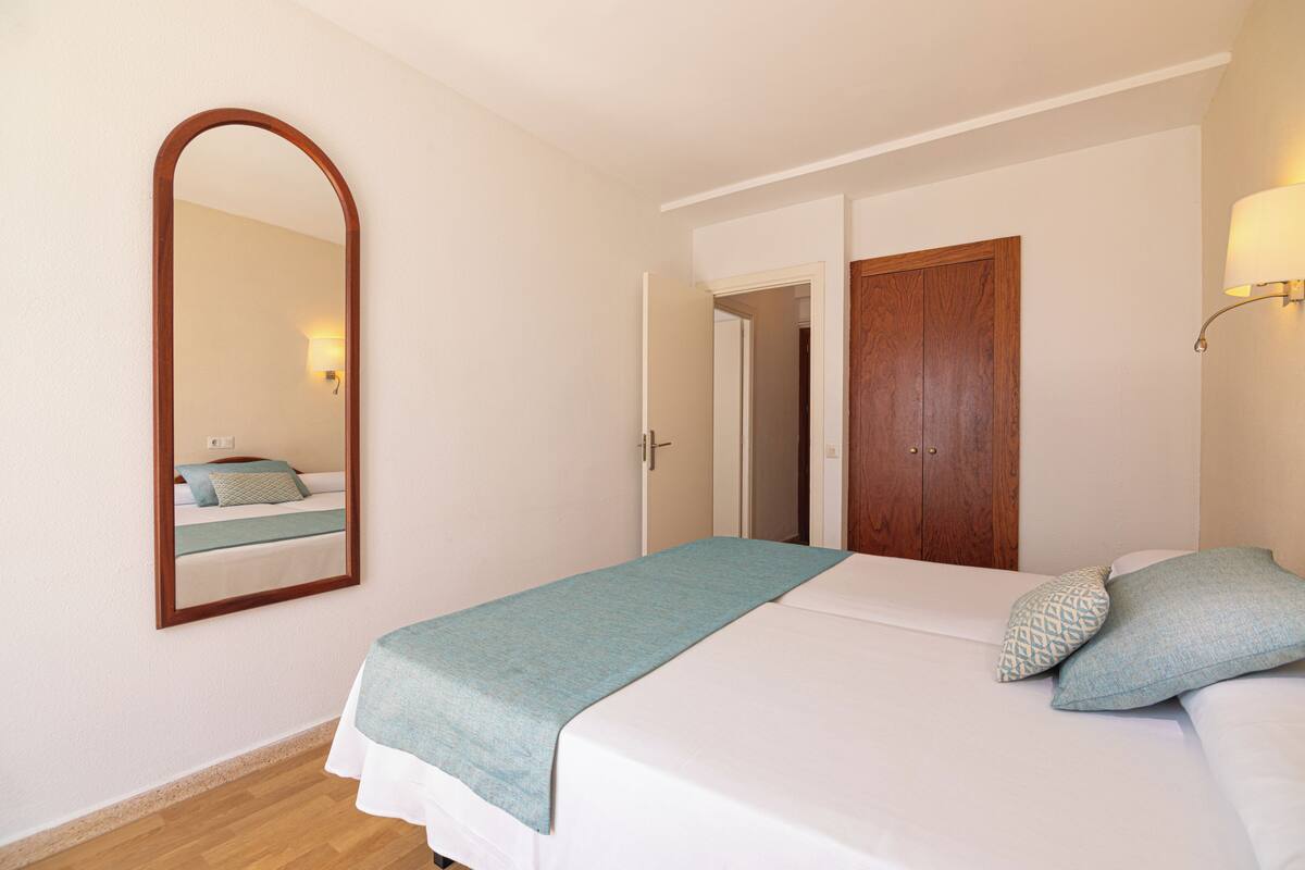 Ein Schlafzimmer mit Bett, Spiegel, Tür und einer wandmontierten Leuchte.