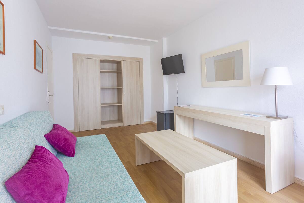 Ein modernes Zimmer mit einer Couch, einem Schreibtisch, einem Fernseher und einem Spiegel.