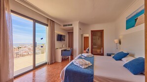 A hotel room with a bed, a desk, a TV, and a view of the city. - Ilusion Markus & Spa (Santa Margalida)