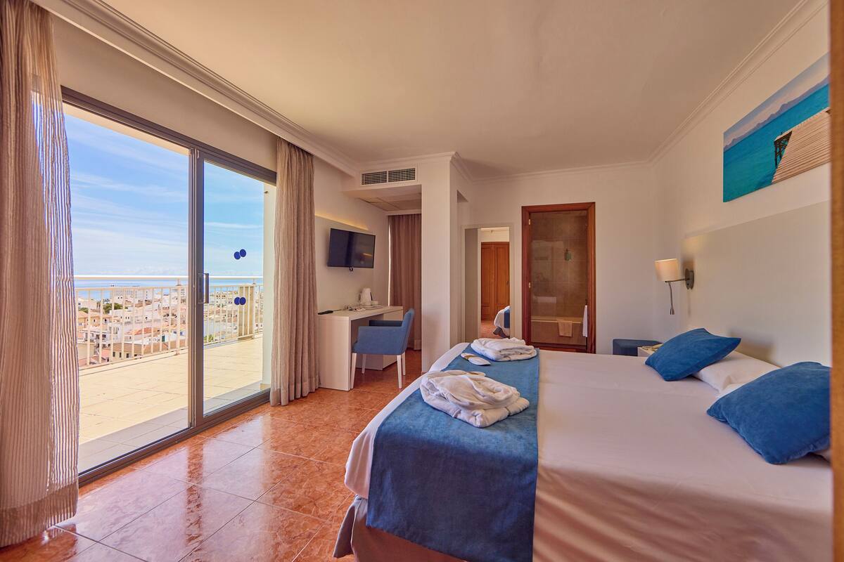 A hotel room with a bed, a desk, a TV, and a view of the city.
