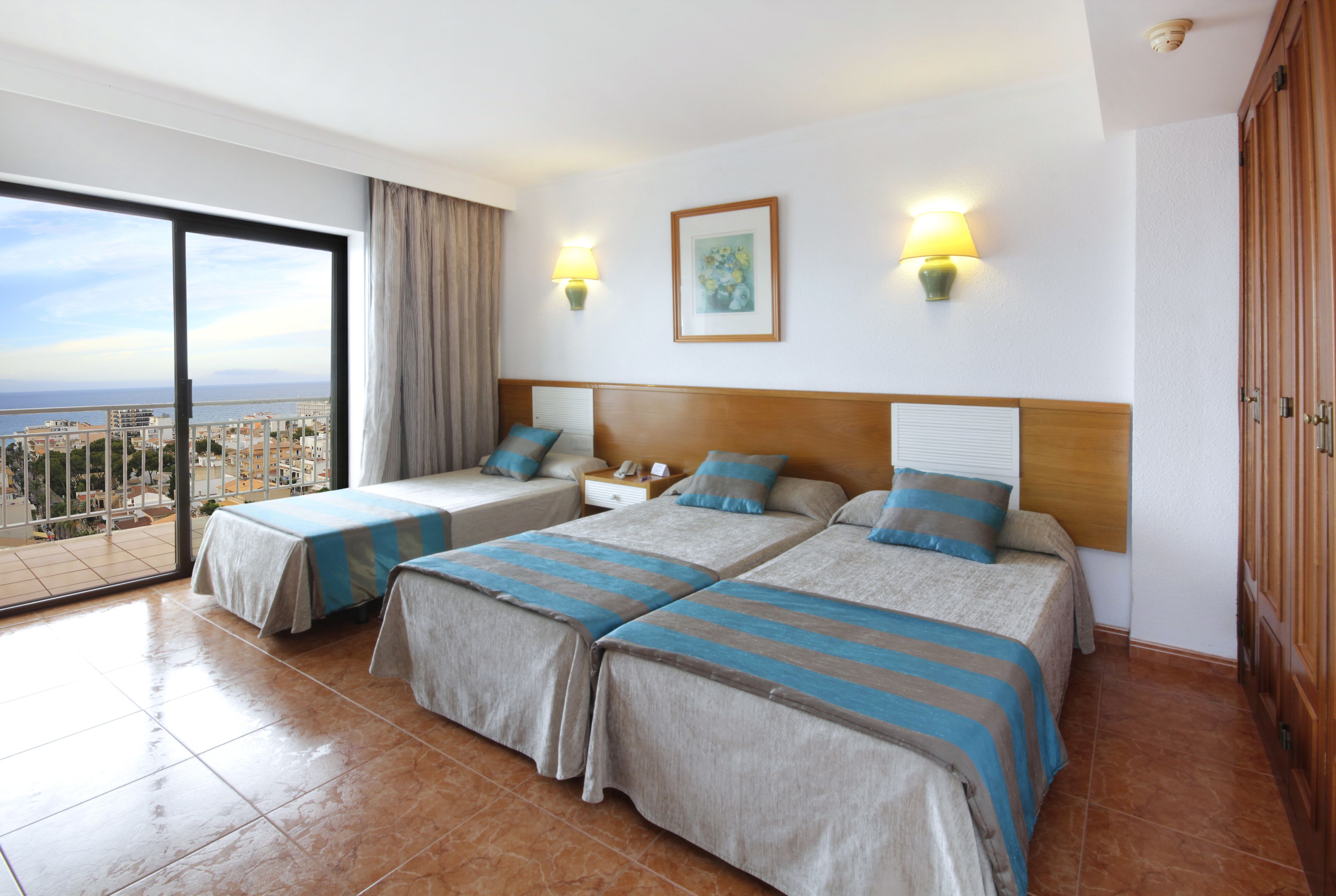 Habitación de hotel con dos camas, un balcón y vista a la ciudad, además de un cuadro en la pared.