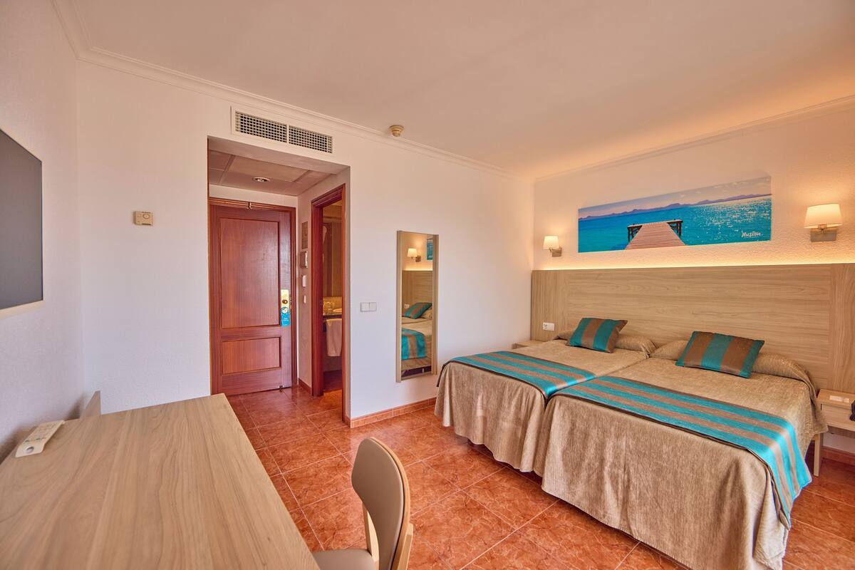 A hotel room with two beds, a wooden headboard, a painting of a beach, a mirror, and a wooden table.
