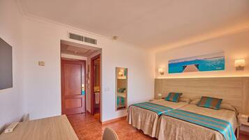 Habitación de hotel con dos camas, cabecera de madera, un cuadro de una playa, un espejo y una mesa de madera.