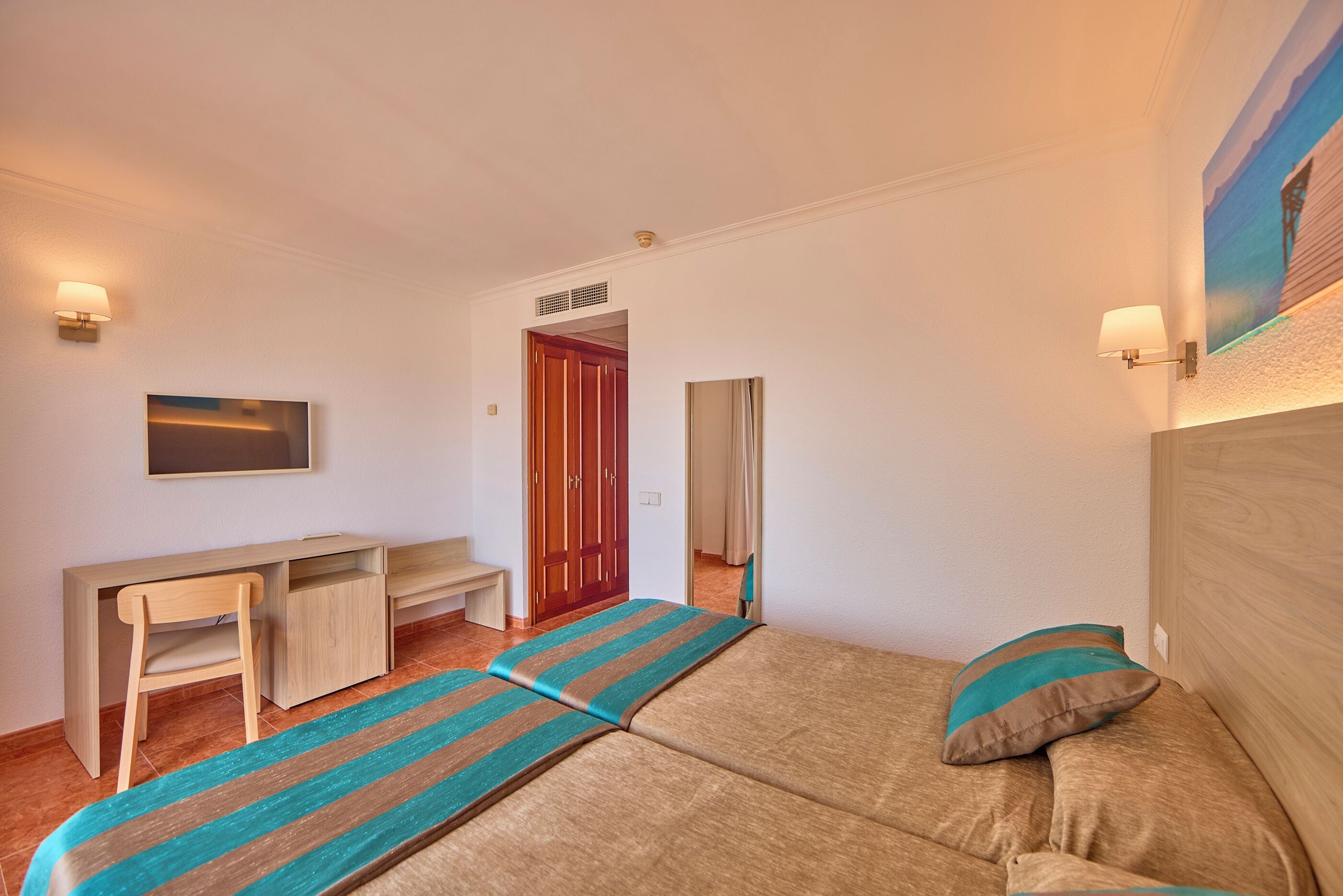 Une chambre à coucher avec un lit, un bureau et une chaise. Une porte donne accès à une autre pièce.
