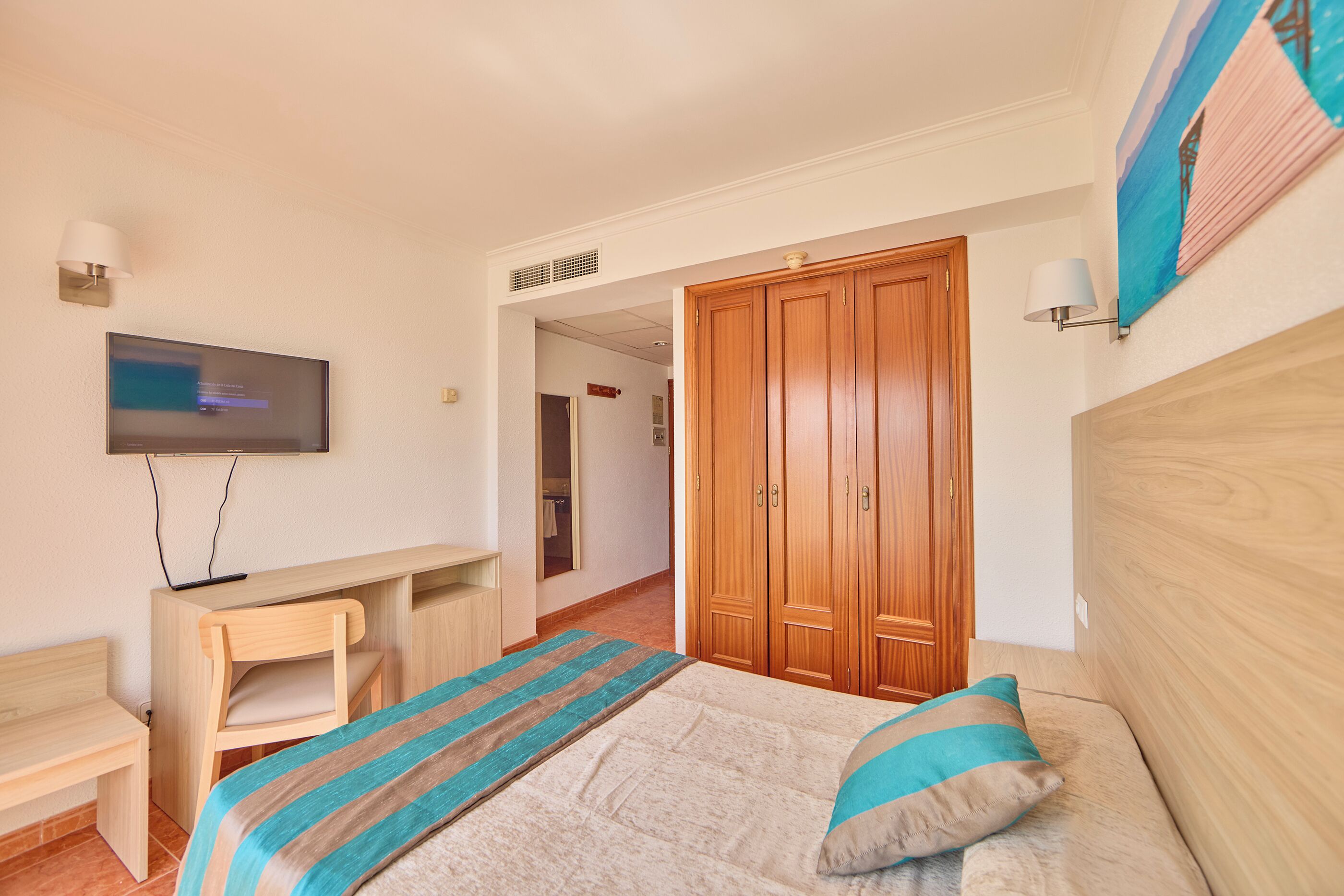 A bedroom with a bed, a desk, a television, and a wardrobe.